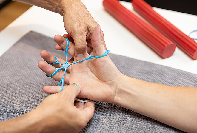 Physiotherapeut unterstützt Patientin bei Handübungen mit Therapiegerät